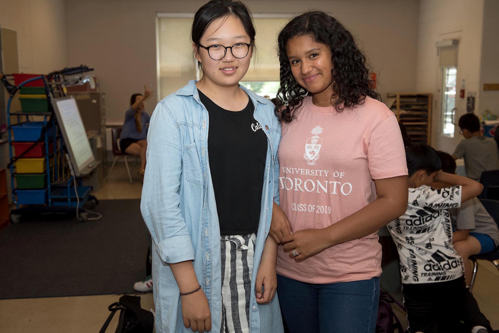 Two students smiling and standing next each other in the classroom Open Gallery